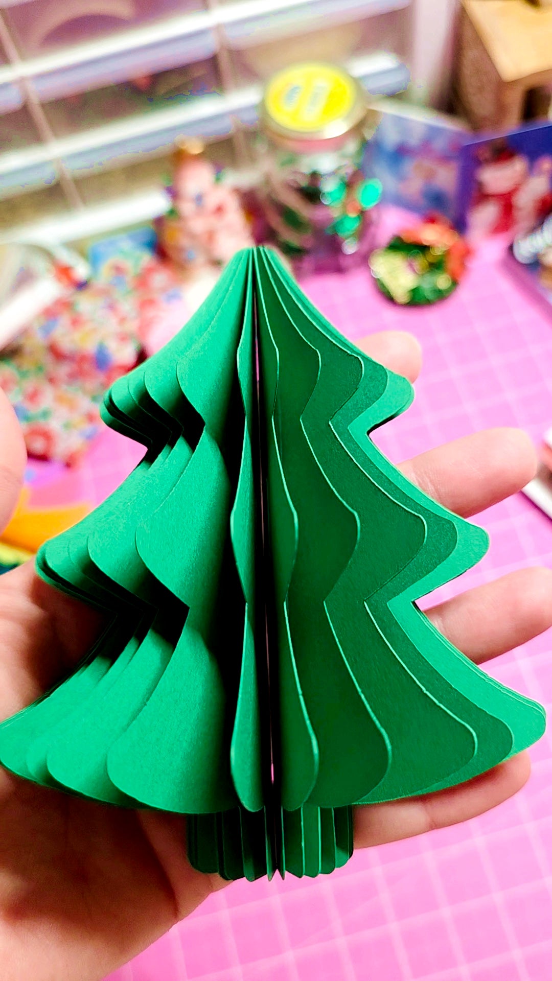Green paper Christmas tree held by a hand with a colorful background