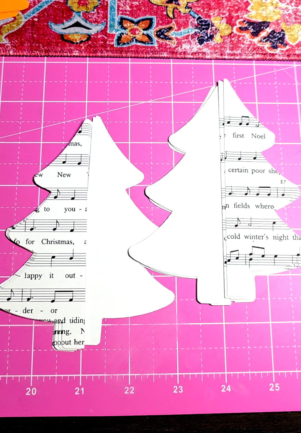 White tree-shaped cutouts with sheet music on a pink cutting mat.