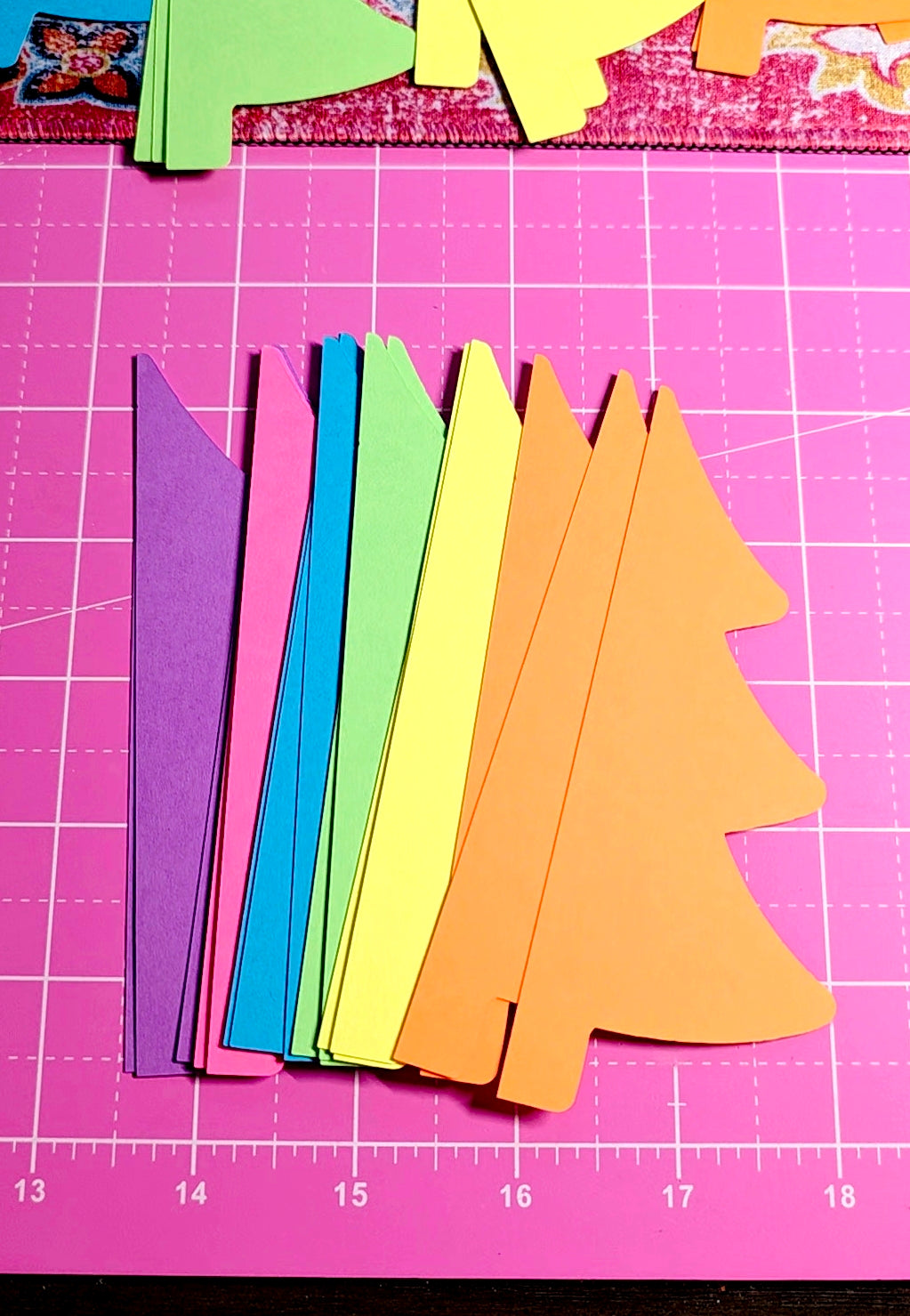 Colorful paper trees on a pink cutting mat with grid lines