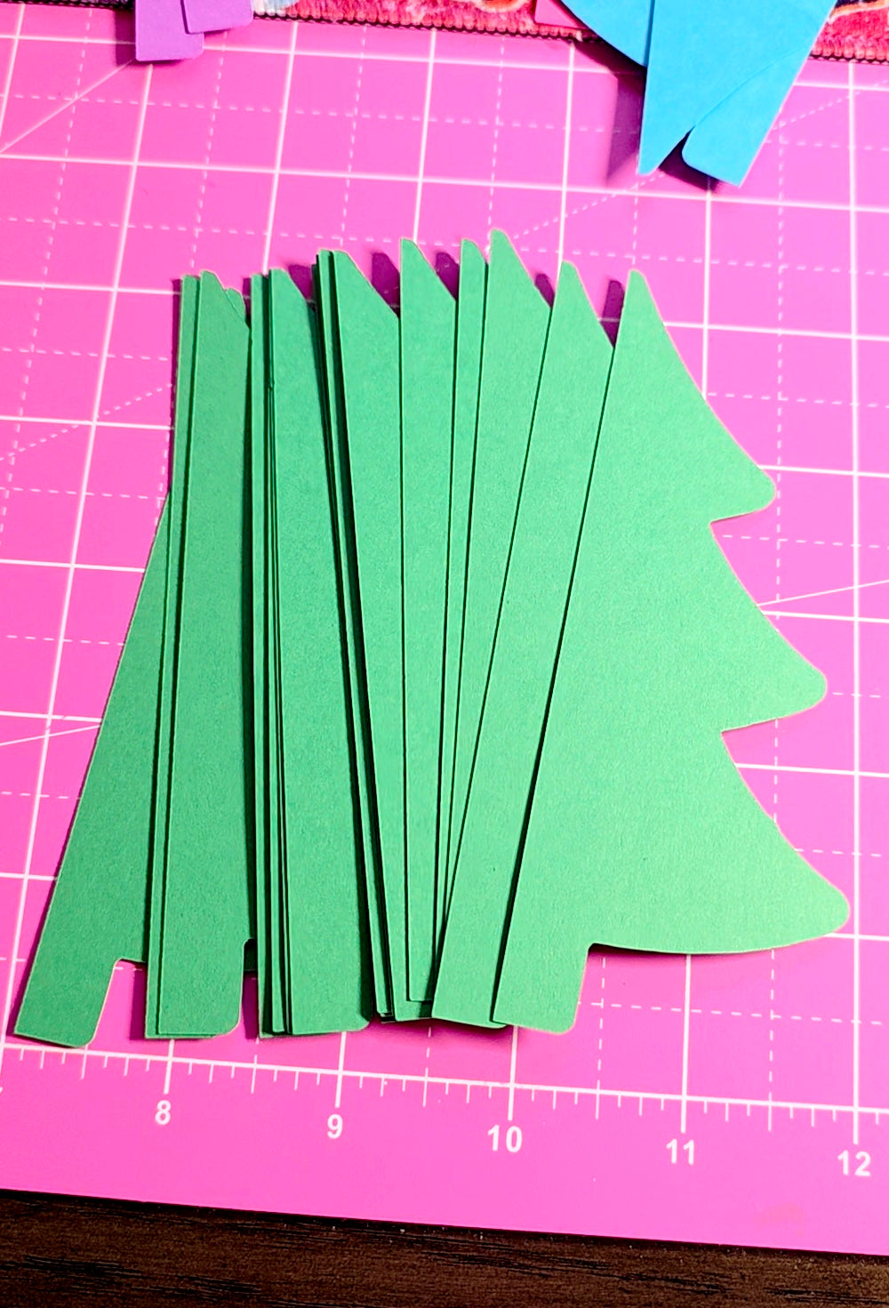 Green paper trees on a pink cutting mat with grid lines
