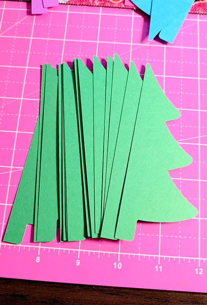 Green paper trees on a pink cutting mat with grid lines