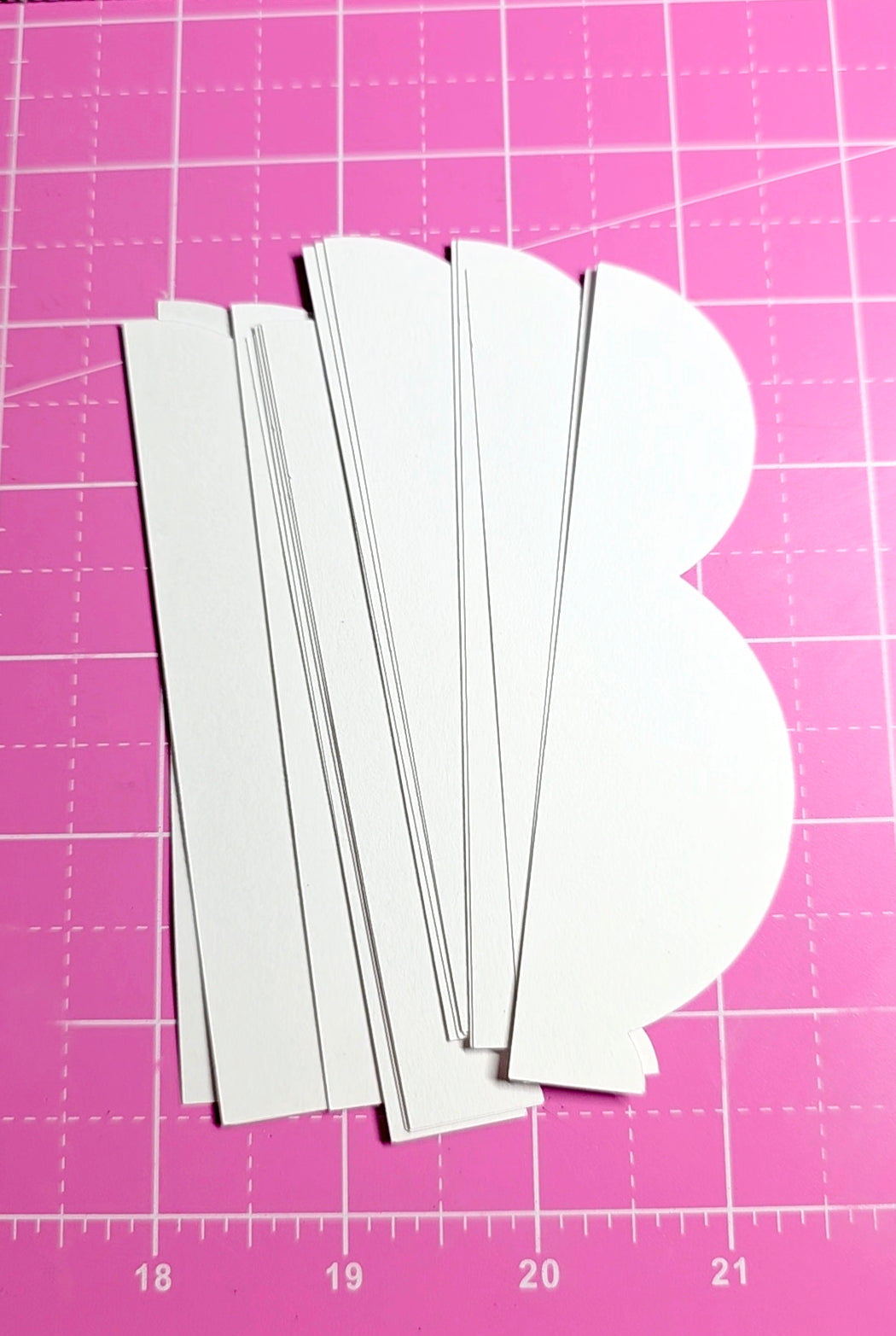 White paper cutouts on a pink cutting mat with grid lines