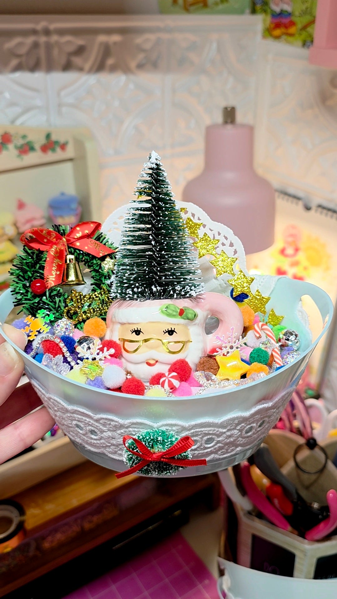 Decorative bowl with small Christmas tree, Santa Claus figure, and colorful ornaments on a blurred background.