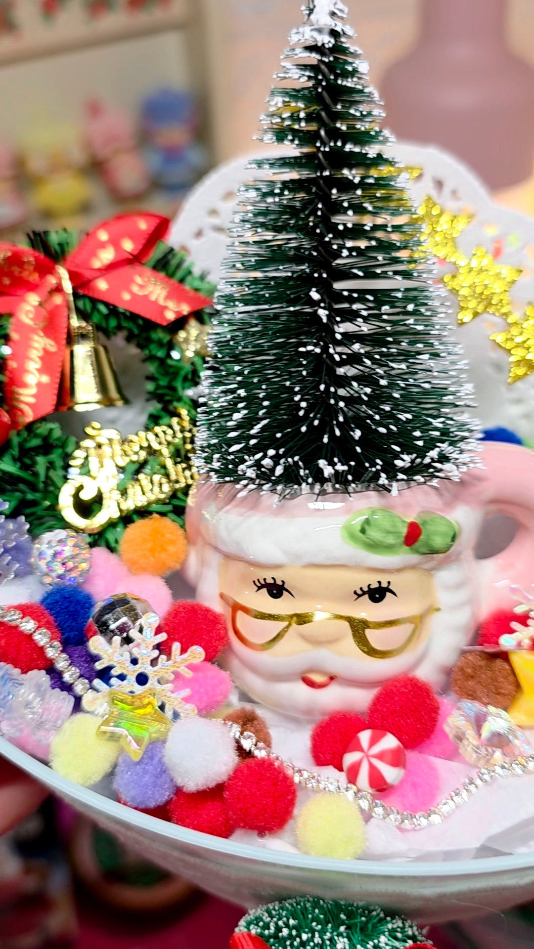 Decorative Christmas scene with a Santa Claus mug, colorful pom-poms, and a small Christmas tree.