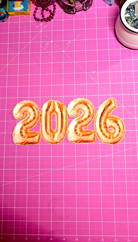 Number '2026' cookies on a pink cutting mat with grid lines