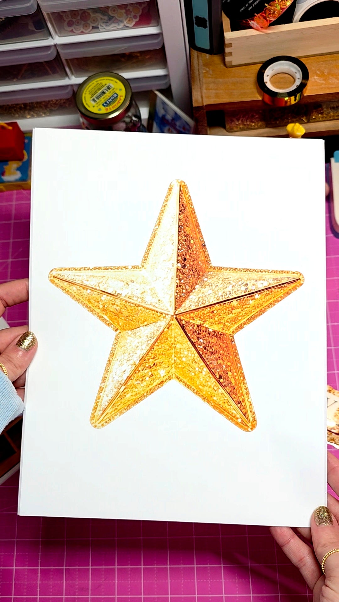 Gold star decoration on a white card held by hands with a crafty background.