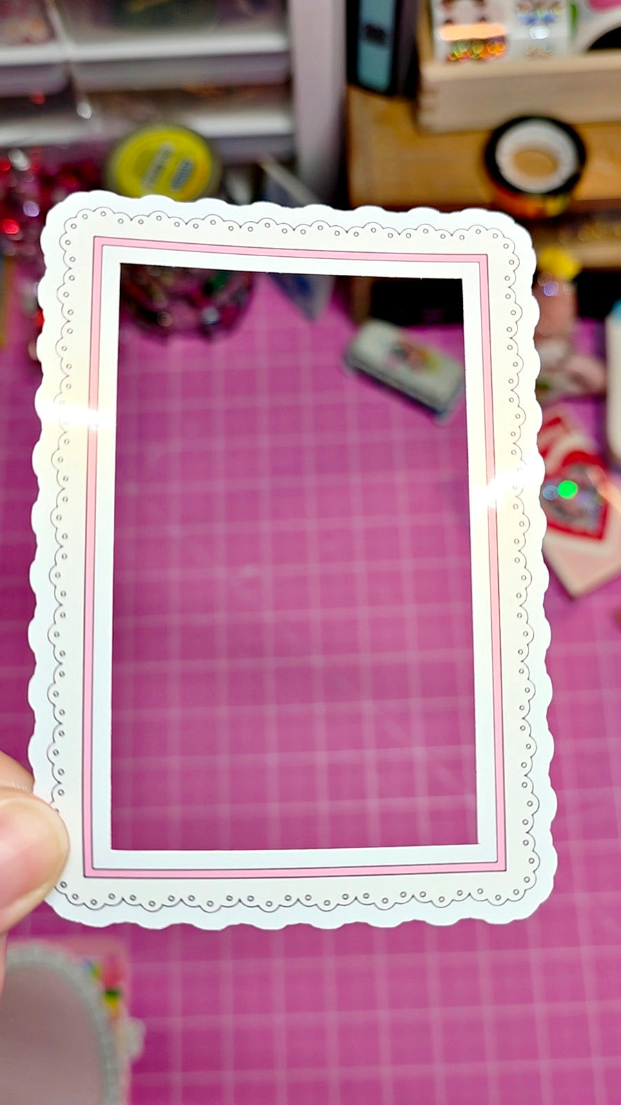 Decorative white frame held over a pink grid background