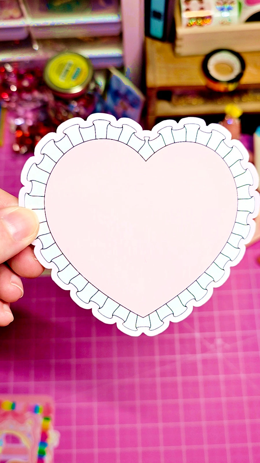 Heart-shaped paper cutout held by a hand on a pink grid background