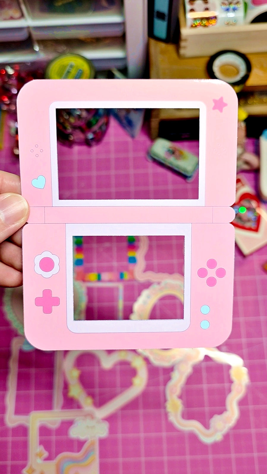 Pink handheld gaming console with a screen displaying colorful graphics, held against a blurred background.