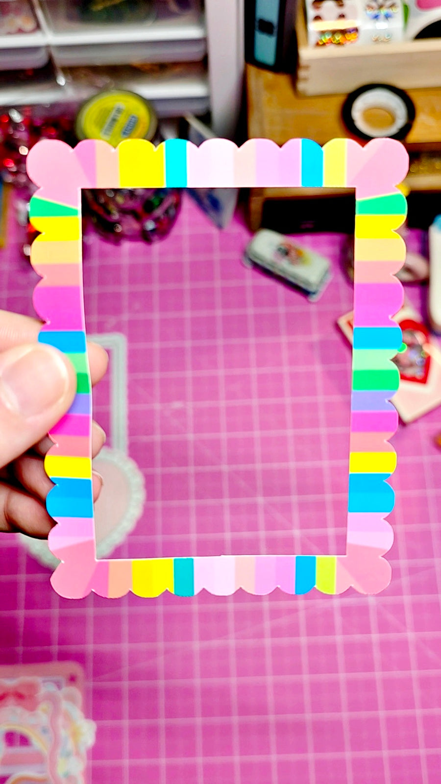Colorful photo frame made of small colorful plastic pieces held over a pink grid background.