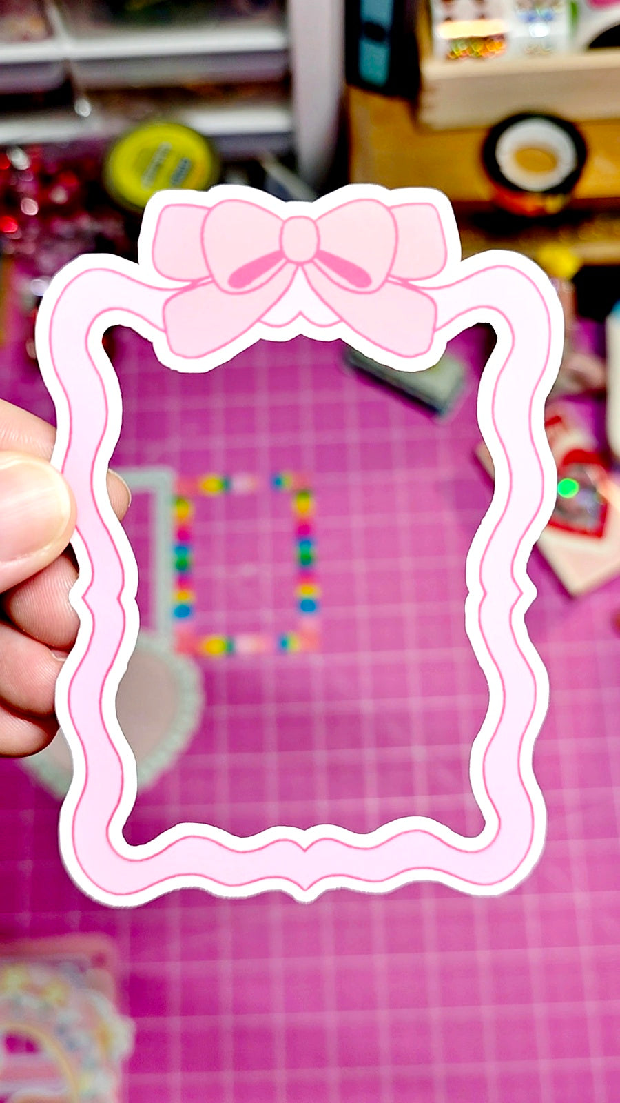 Pink decorative frame with a bow held against a colorful, blurred background
