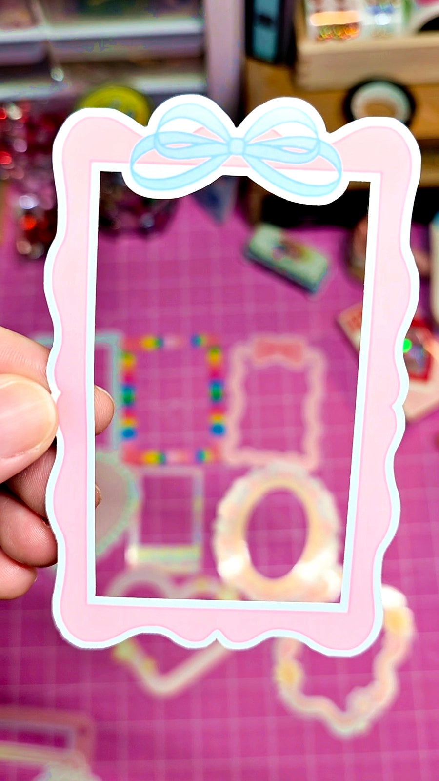 Decorative photo frame with a bow held by a hand on a pink background.