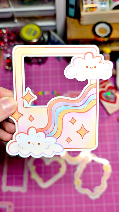 Decorative phone case with cloud and rainbow design held by a hand on a pink surface.