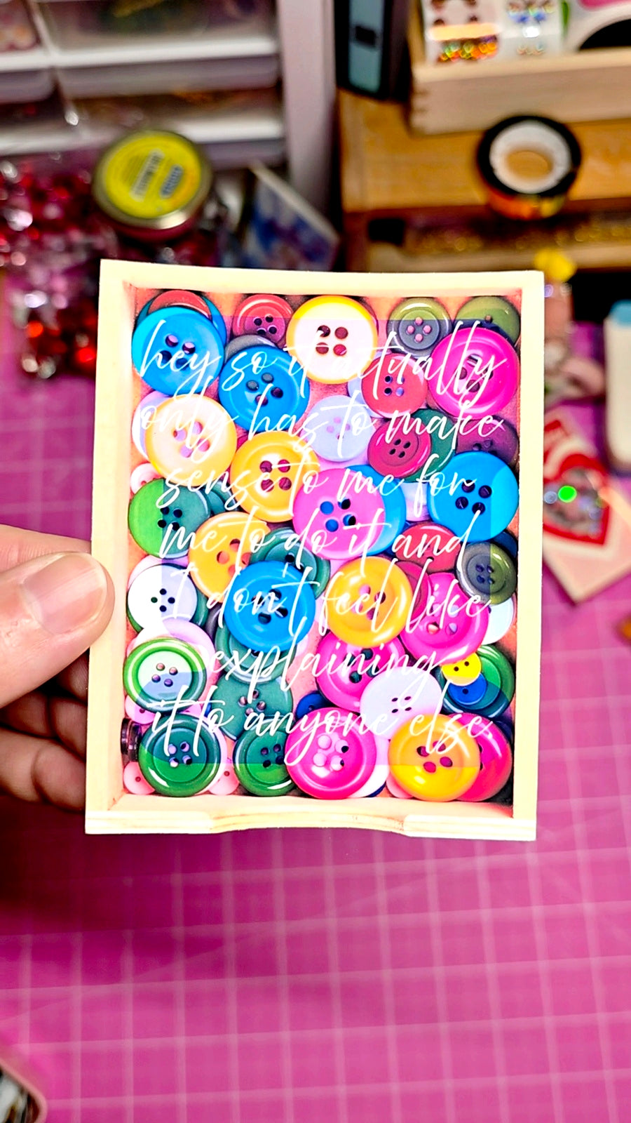 Colorful button assortment on a card held over a pink grid background