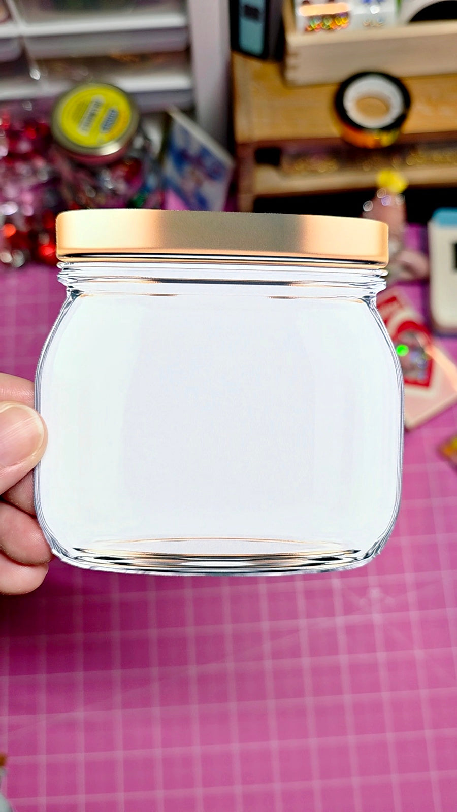 Clear jar with gold lid held by a hand against a colorful background