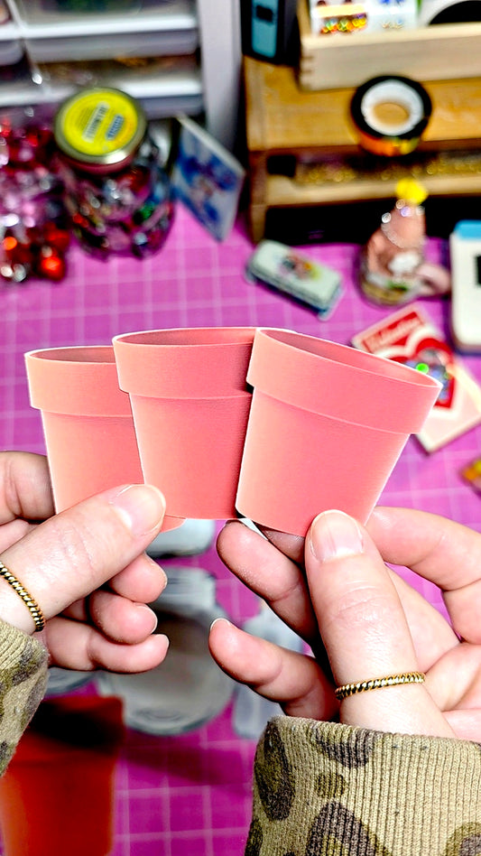 Three pink flower pots held by hands against a colorful background