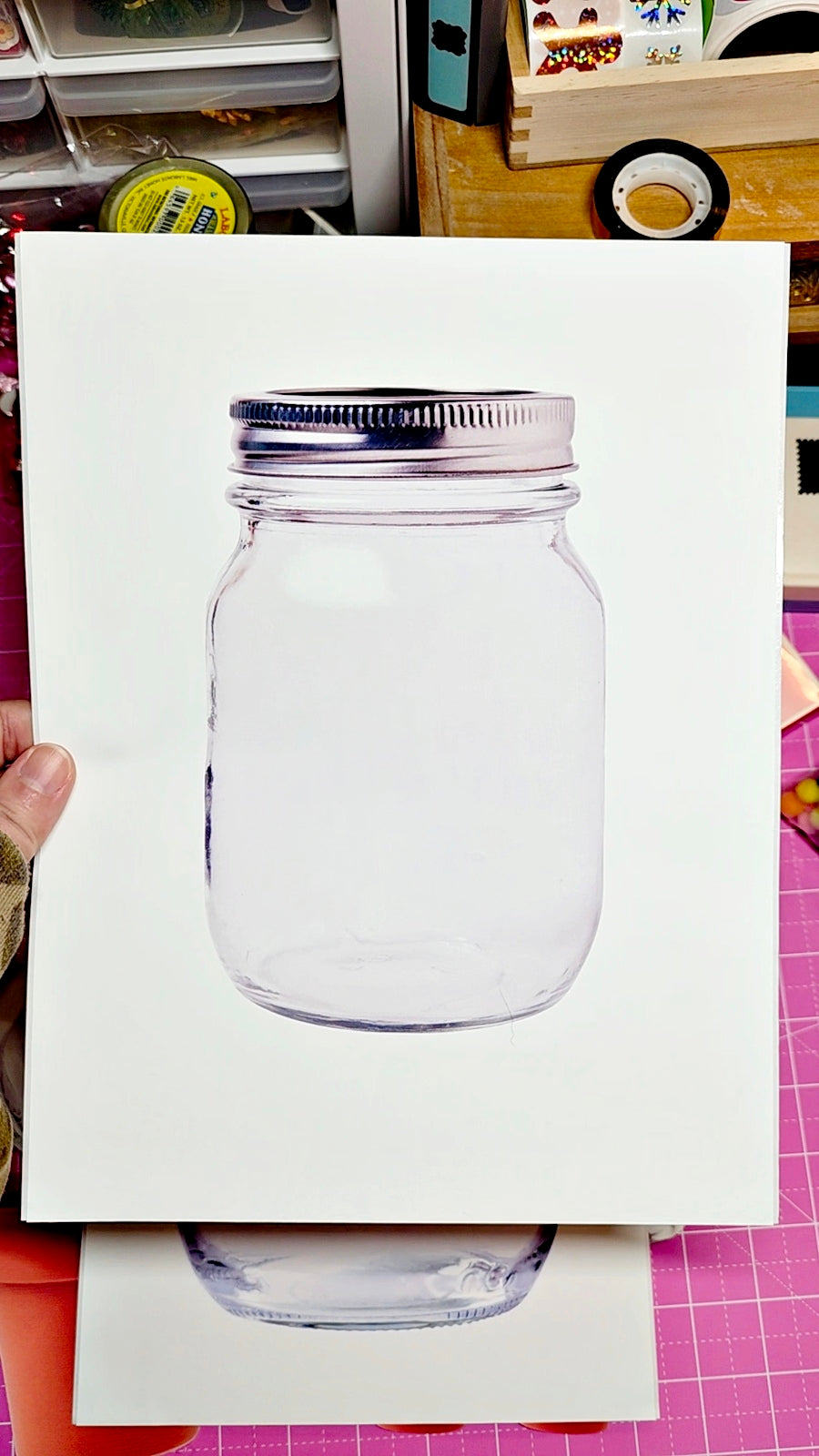 Clear glass jar with a silver lid on a white card, held against a colorful background.