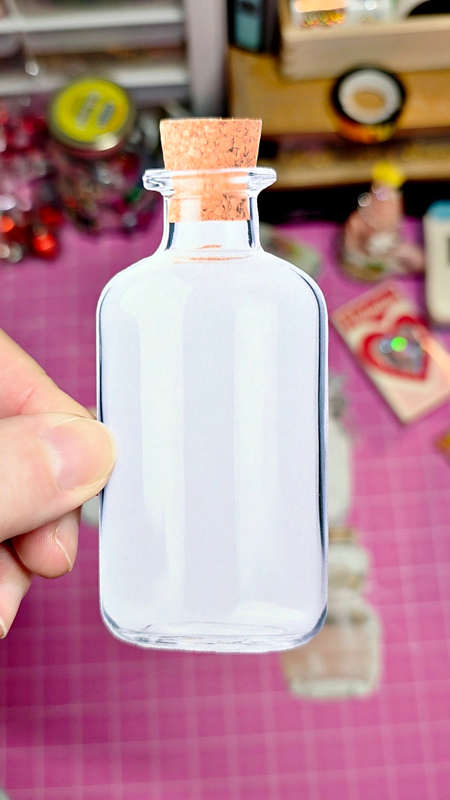 Clear glass bottle with cork stopper held by a hand against a colorful background