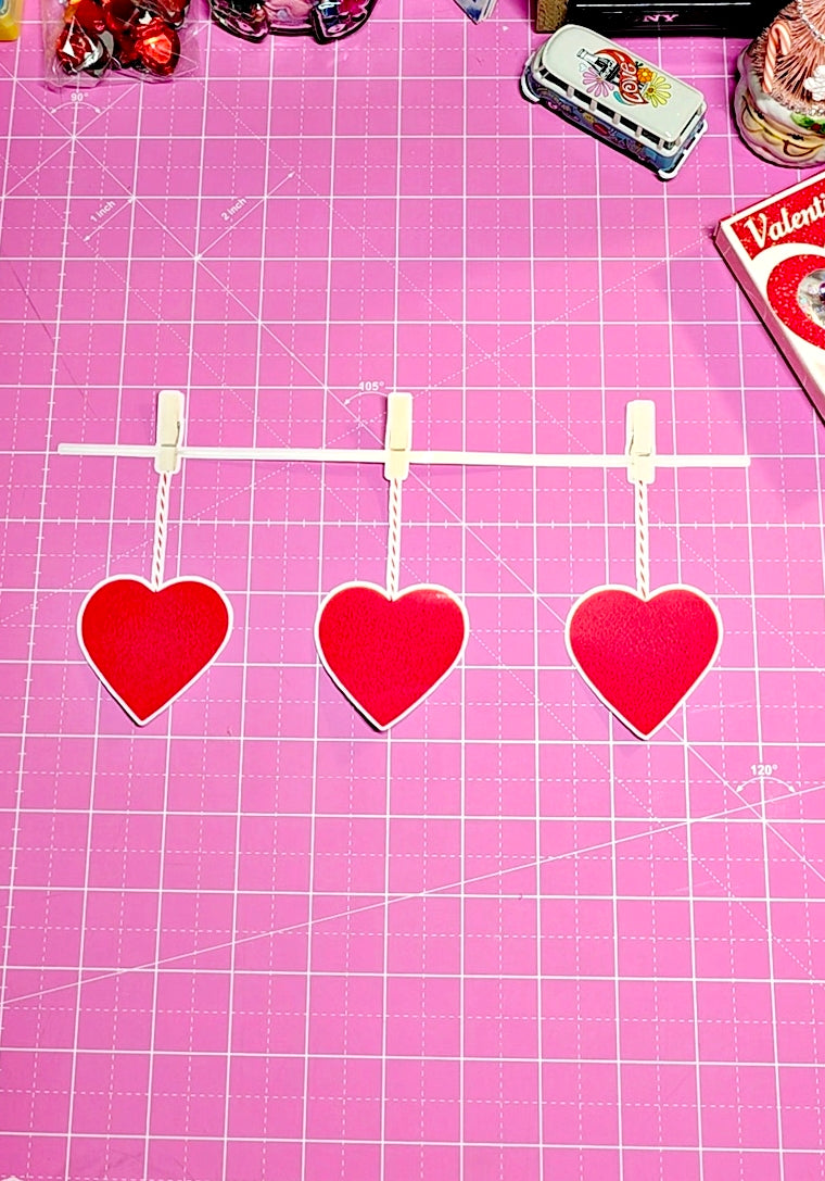 Red heart-shaped decorations on a pink cutting mat with grid lines.