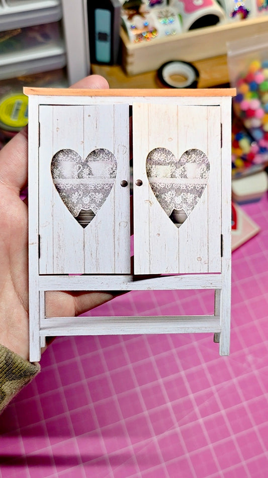 Small wooden cabinet with heart-shaped cutouts on a pink surface