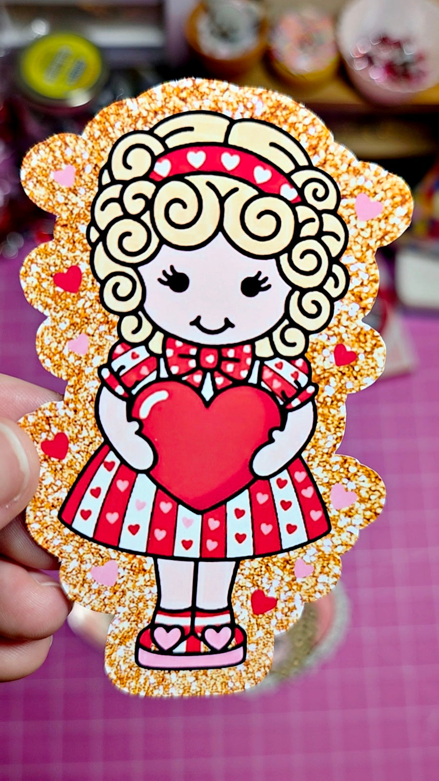 Decorative sticker of a cartoon character holding a heart with gold glitter border.