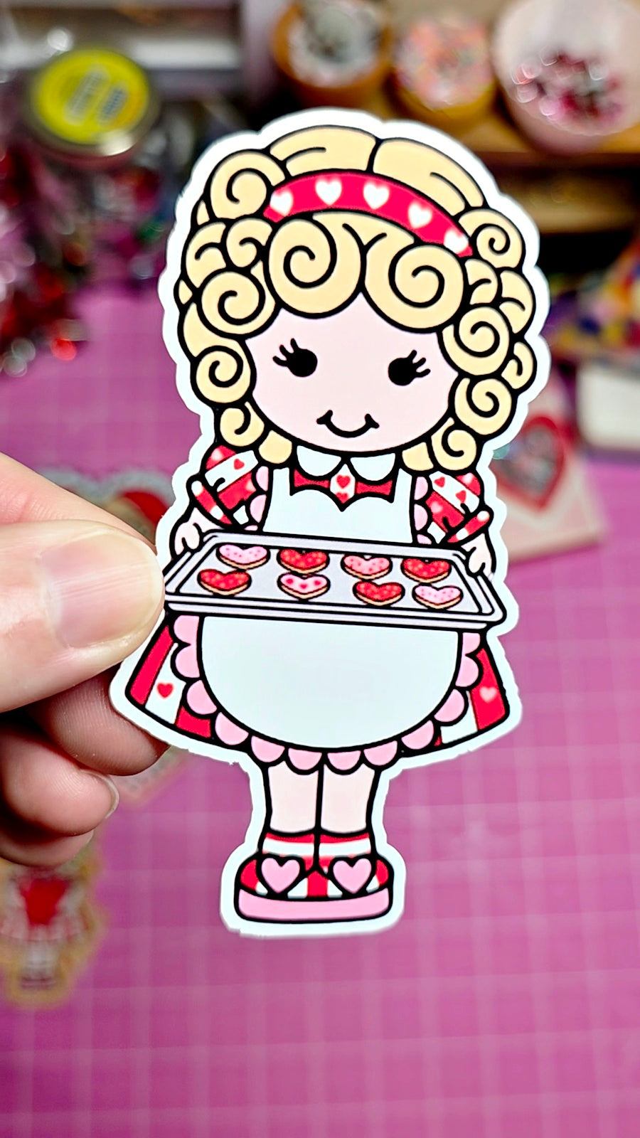 Cartoon character sticker held by a hand on a pink background