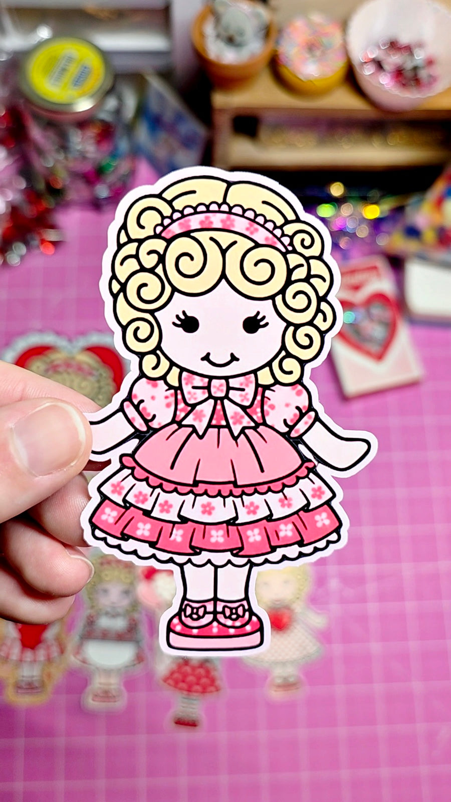 Cartoon character sticker of a girl in a pink dress held over a colorful background with toys.