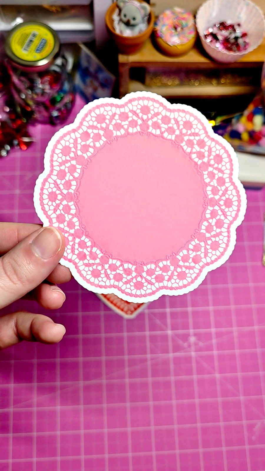 Pink paper doily held by a hand on a pink grid background