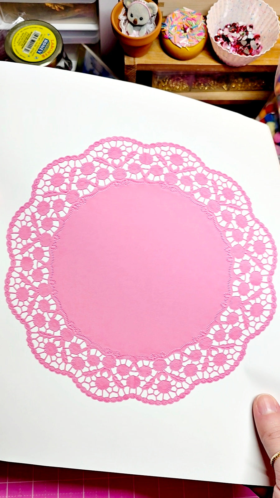 Pink paper doily on a white sheet of paper with a blurred background