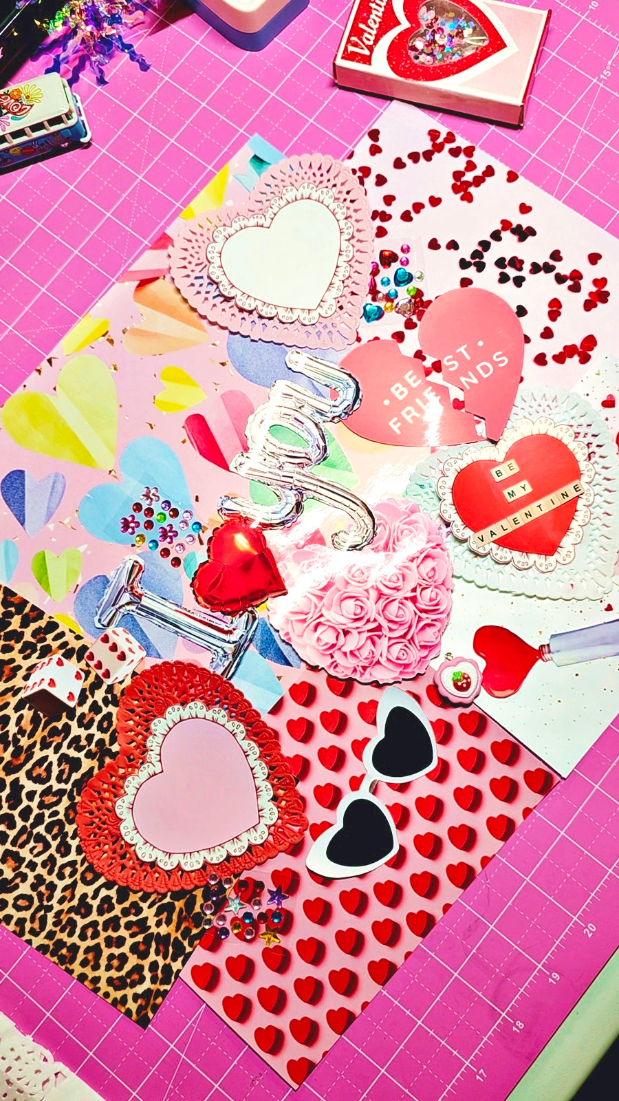 Valentine's Day-themed stationery items on a pink cutting mat with grid lines.