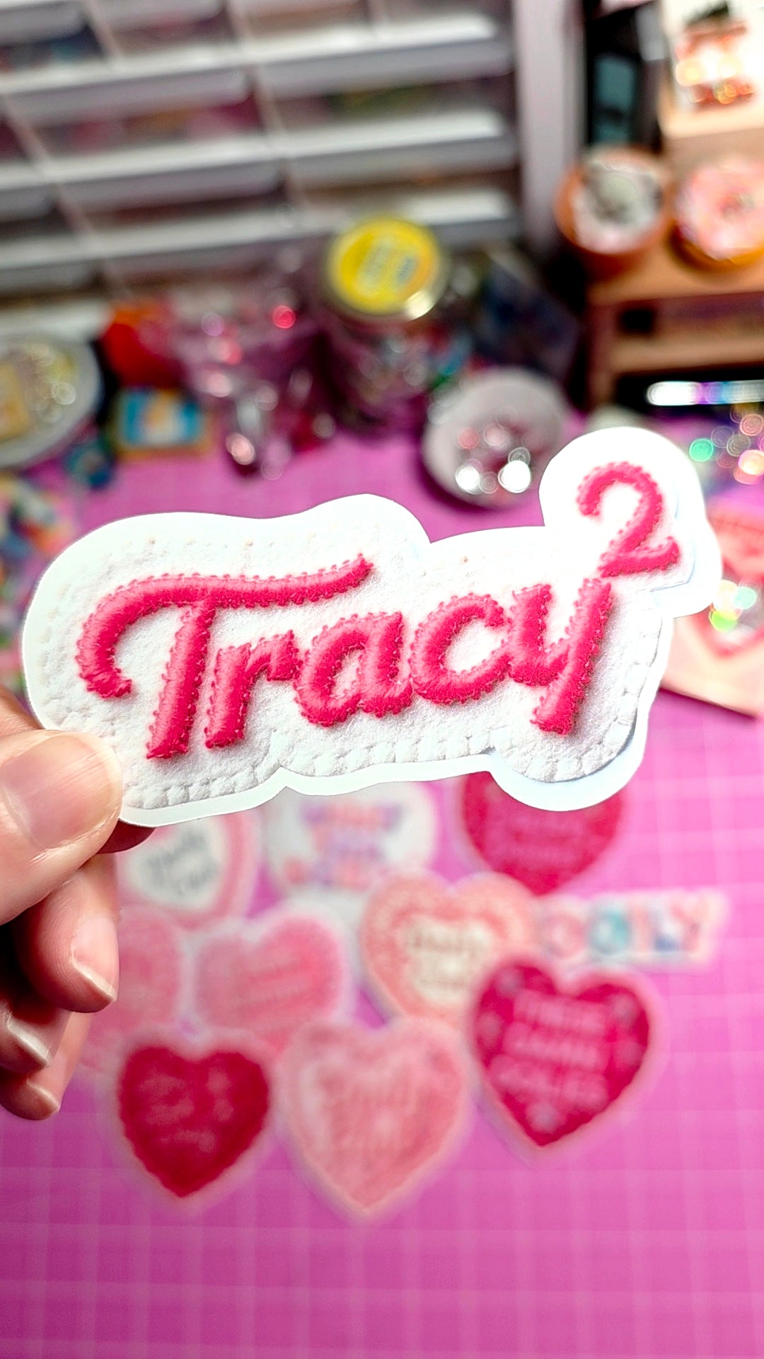 Patch with 'Tracy' in pink letters held over a colorful background