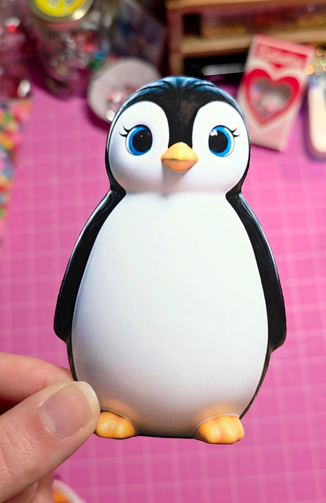 Toy penguin held by a hand against a pink background