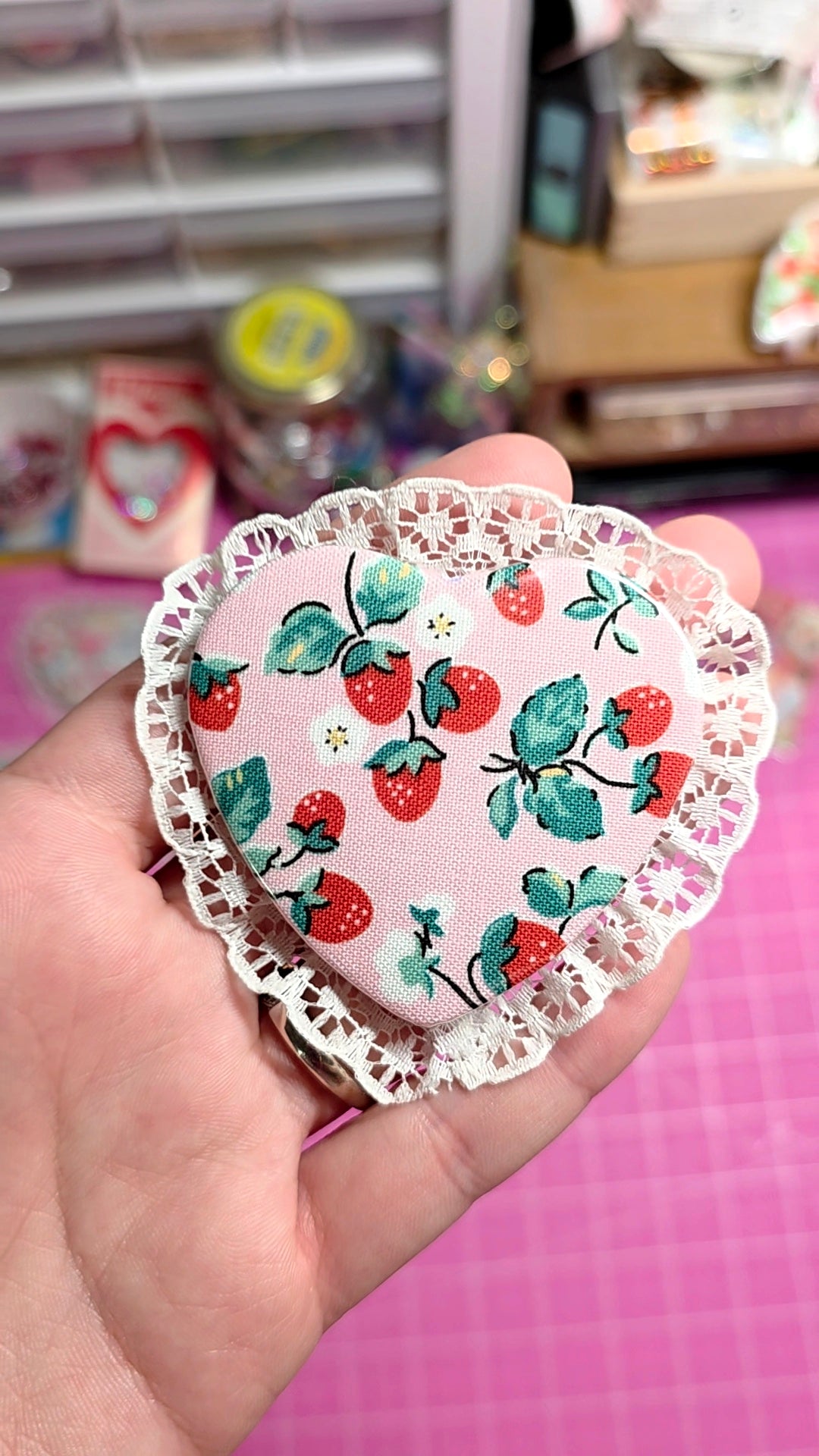 Heart-shaped doily with strawberry pattern held in a hand against a blurred background