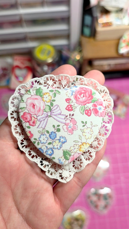 Decorative heart-shaped sticker with floral design held by a hand against a blurred background