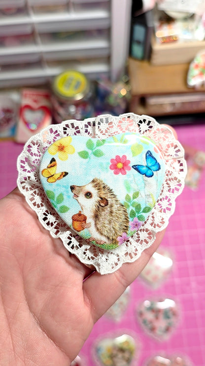 Heart-shaped sticker with a hedgehog design held by a hand against a blurred background