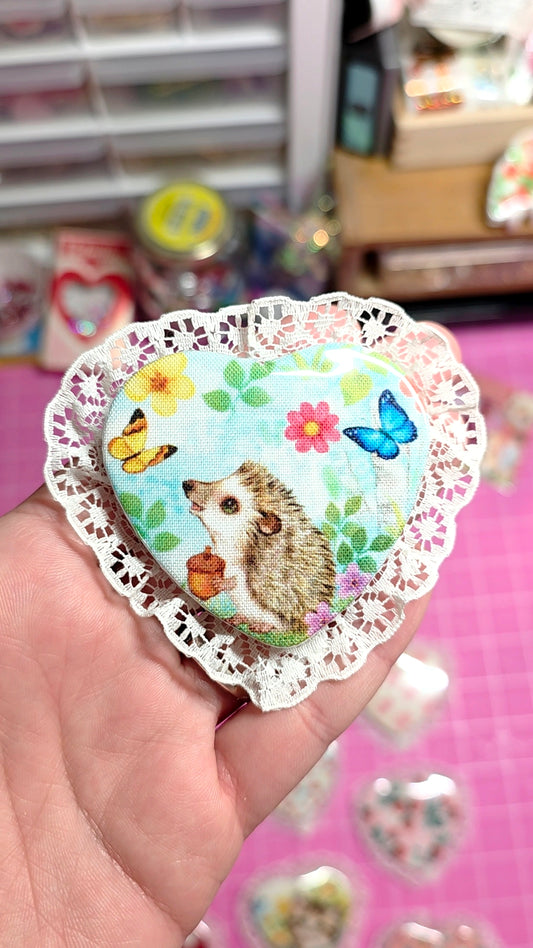 Heart-shaped sticker with a hedgehog design held by a hand against a blurred background