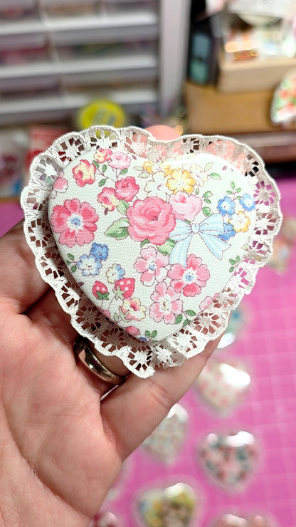 Heart-shaped decorative item with floral pattern held by a hand against a blurred background