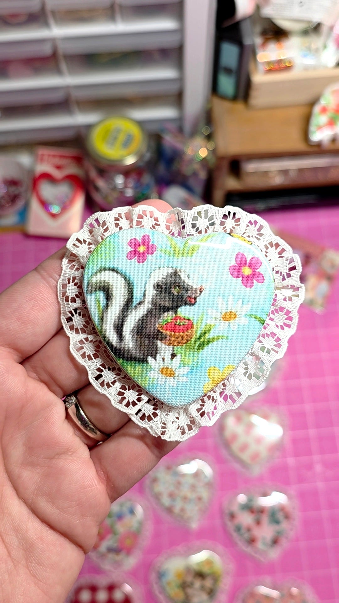 Decorative sticker with a skunk design held by a hand on a pink surface.