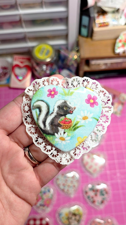 Decorative sticker with a skunk design held by a hand on a pink surface.