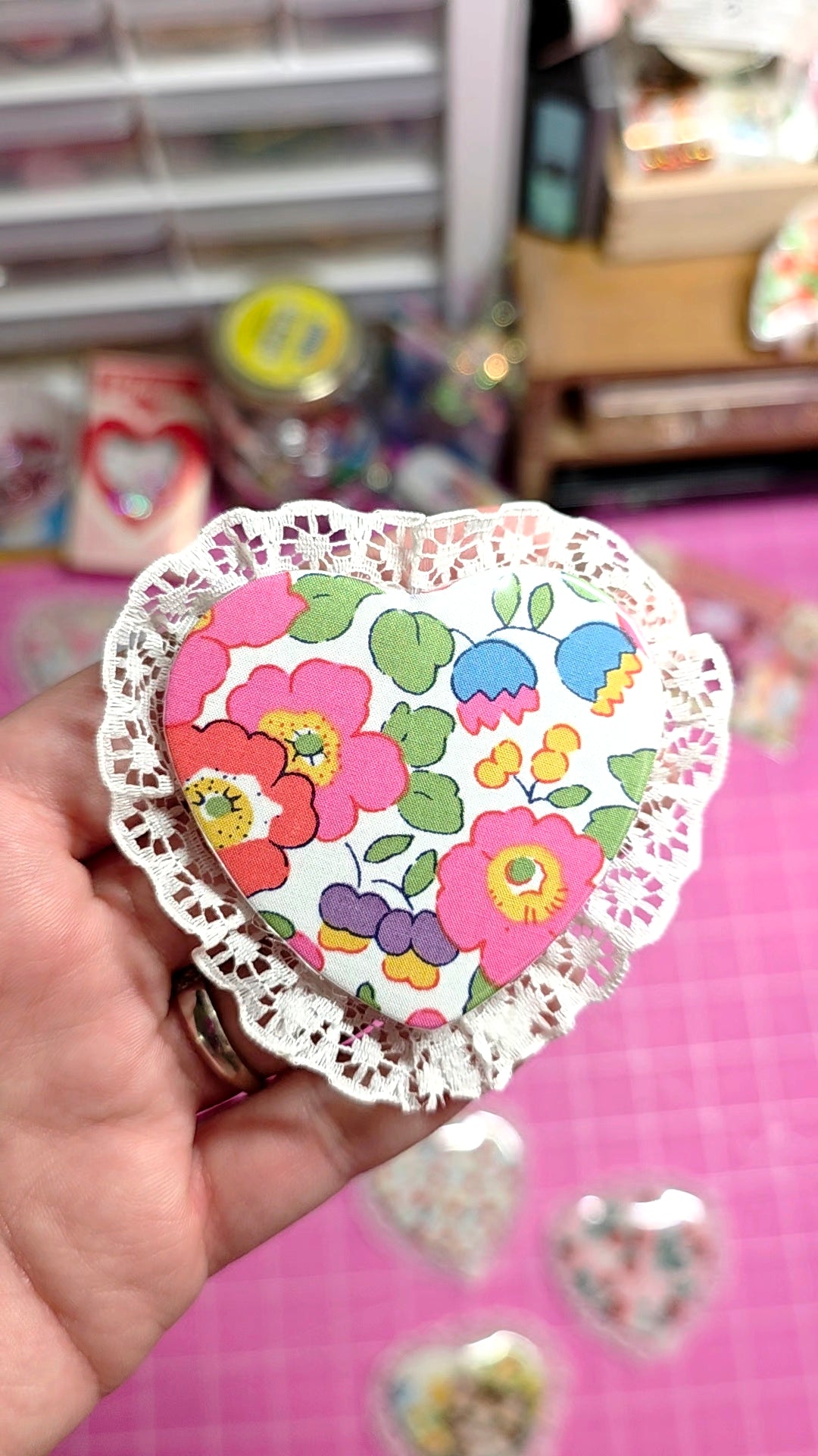 Heart-shaped paper cutout with colorful floral design held by a hand on a pink surface.