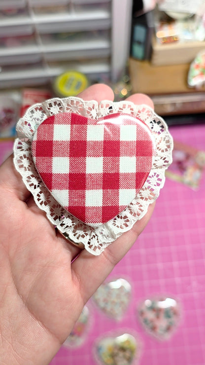 Heart-shaped fabric pin with checkered pattern and lace trim held in a hand.