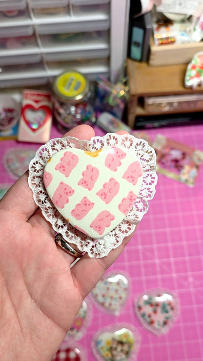 Heart-shaped pink candy with decorative lace border held by a hand on a pink surface.