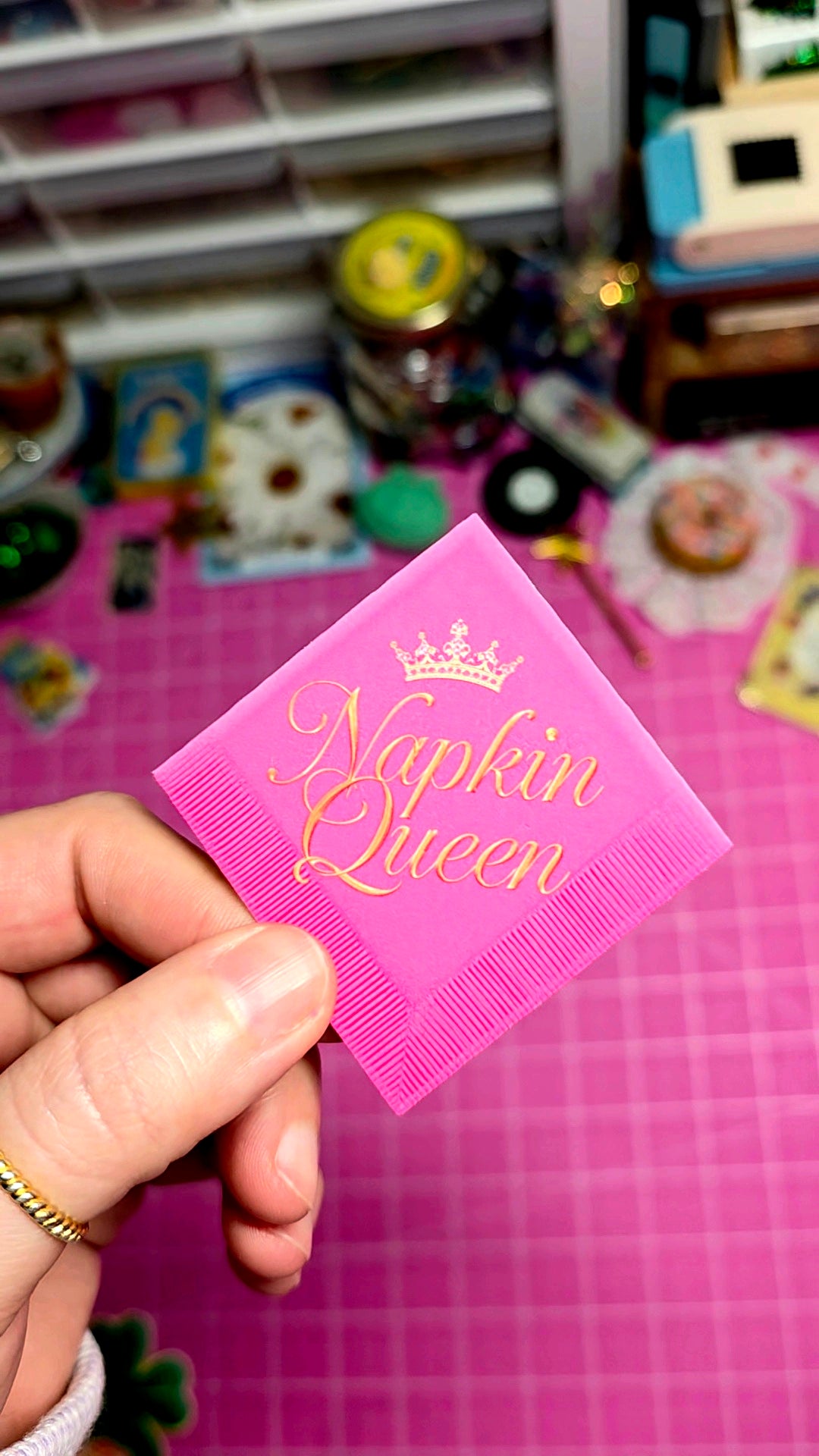 Pink napkin with 'Napkin Queen' text held by a hand against a colorful background