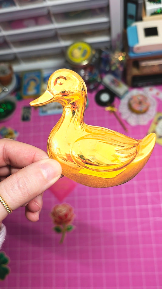 Gold duck-shaped object held by a hand with a colorful background