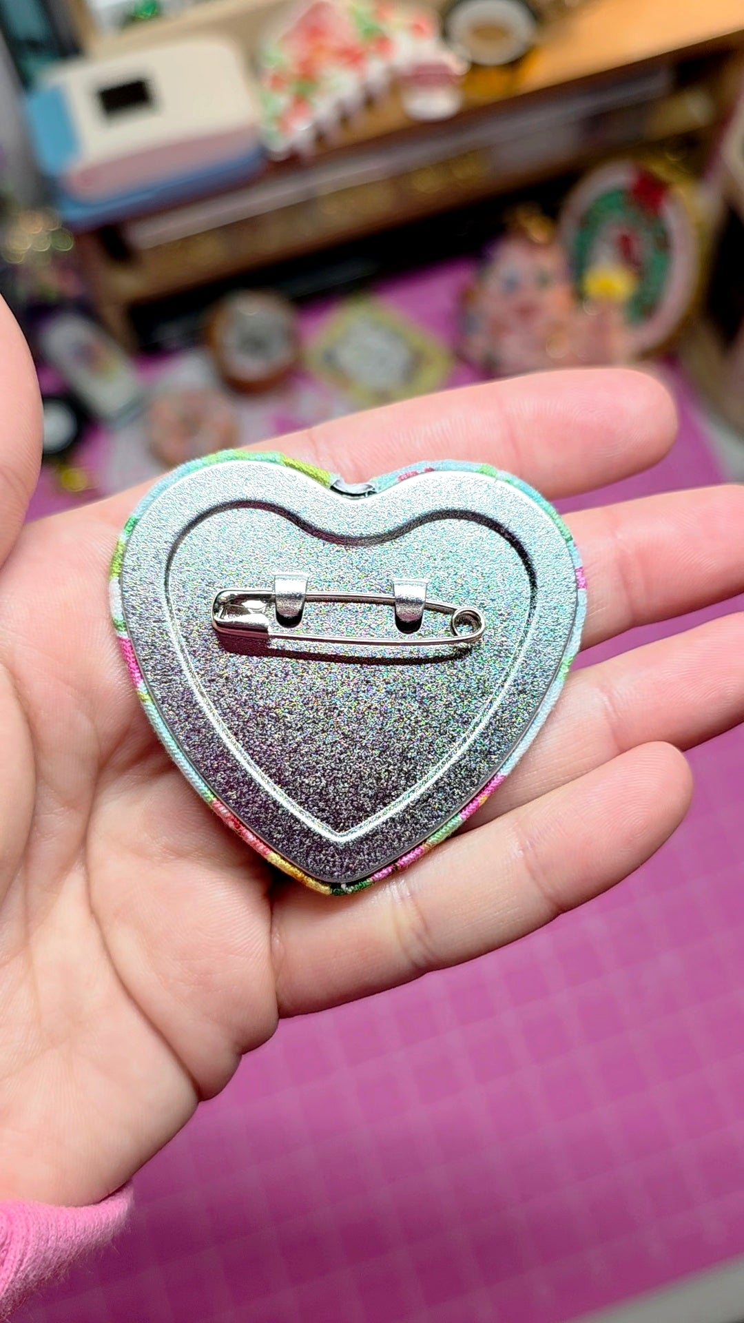 Heart-shaped glittery pin held in a hand with a blurred background