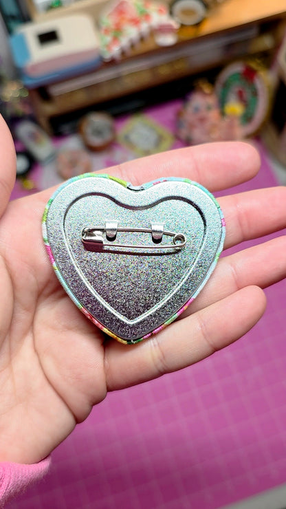 Heart-shaped glittery pin held in a hand with a blurred background