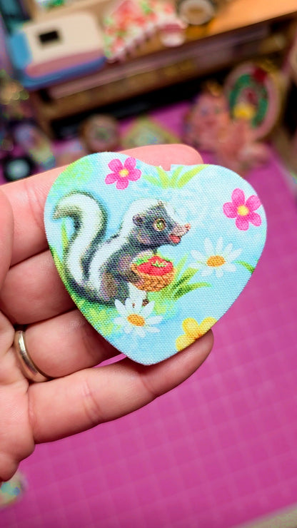 Hand holding a colorful patch with a skunk design against a pink background