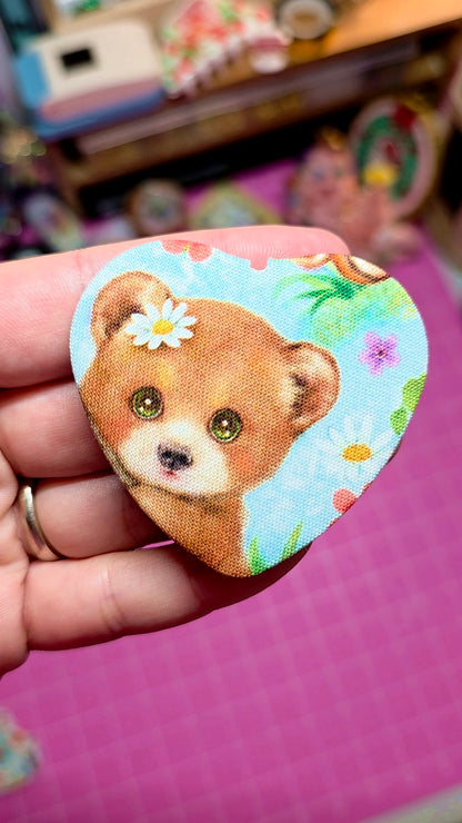 Fabric patch of a bear with flowers held by a hand on a pink surface.
