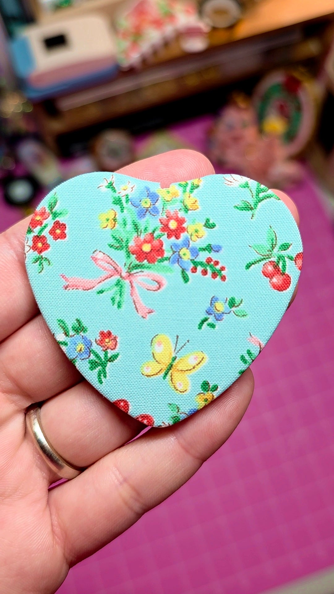 Heart-shaped fabric patch with floral and butterfly design held in a hand.