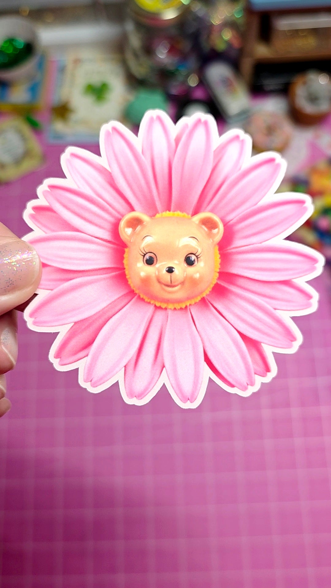 Pink flower-shaped object with a bear face on a pink background